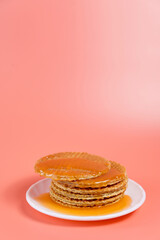 Stack of stroopwafels with melted caramel dripping on plate over pink background