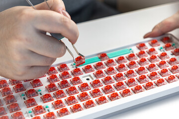 Close-up of person removing red switch from mechanical keyboard using tool during customization