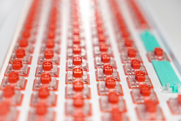 Rows of red hot-swap mechanical keyboard switches aligned on white PCB plate during assembly