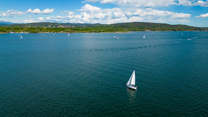 Arona,  Lake Maggiore, Italy: A sailboat glides gracefully across a serene lake under a bright blue...