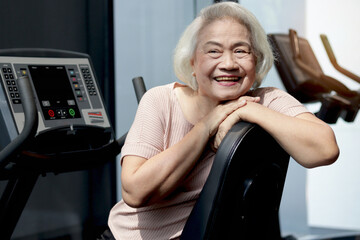 Portrait of happy smiling elderly Asian woman with exercise machine at indoor gym. Joyful senior...