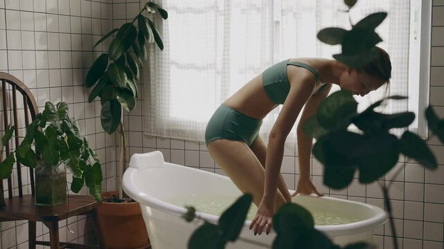 A young Asian woman doing an ice bath or cryotherapy in the home bathroom.