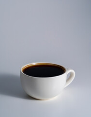 White ceramic cup with black coffee on light gray background