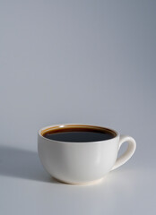 White cup filled with black coffee on soft gray background