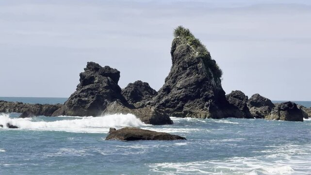 Powerful waves crash against towering rocky formations at Monro Beach, a famous spot to see rare Fiordland crested penguins (tawaki), West Coast,  Haast, New Zealand.