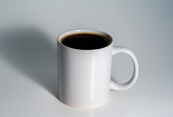 White ceramic mug filled with black coffee on white background