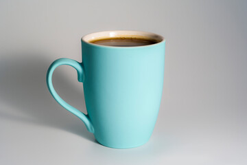 Turquoise ceramic mug filled with coffee on light background
