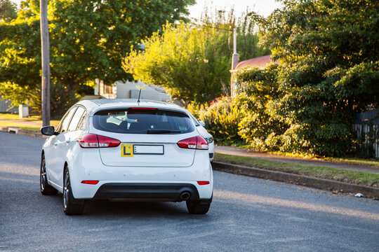 White car with l plate driving on quiet suburban road