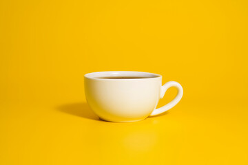 White ceramic cup with tea on bright yellow background