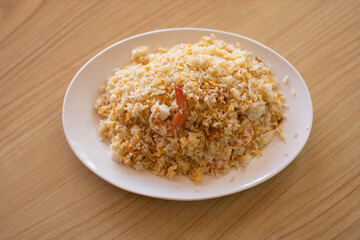 Shrimp fried rice in a white plate placed on a wooden table.