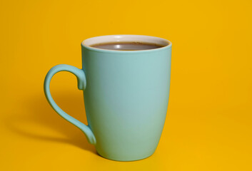 Blue ceramic coffee mug with drink on yellow background