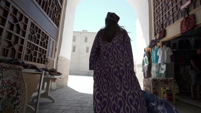 A young woman with long hair in an oriental robe and a skullcap walks through an ancient oriental city