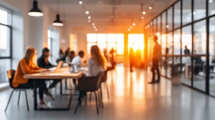 Blurred image of a modern office with employees working, bathed in warm sunlight during the day.