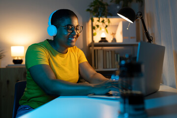 Young Black woman working from home at night listening music with headphones