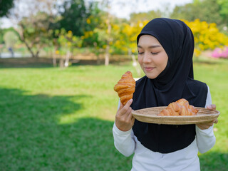 Young lady holding croissants tray in the park, surrounded by nature, perfect for lifestyle,...