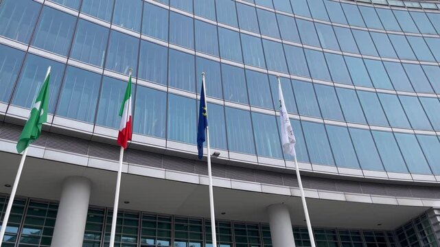 Facade of the Palazzo Lombardia, the Lombardy Regional Government headquarters in Milan, Italy. Flags of Lombardy, Italy, the European Union, and the Olympic Committee by the modern glass building