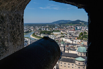 Cannon view from Hohensalzburg Fortress overlooking the historic old town of Salzburg, Austria, with scenic rooftops, the Salzach River, and distant hills under a clear blue sky.