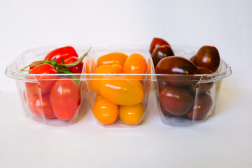 Front view of ripe multicolored tomatoes in clear plastic container isolated on white. Tricolor of Cherry tomatoes. Plum tomatoes from supermarket.