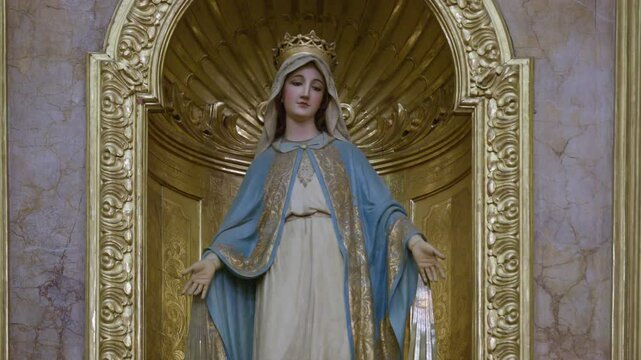 Devotional statue of the Virgin Mary, possibly representing the Virgin of the Miraculous Medal, standing within a richly decorated gilded niche or alcove.