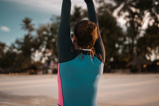 Surfer woman wearing a wetsuit stretching on the beach at sunset - Powered by Adobe