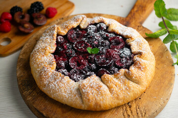 Galette tart with red berries, cherries, raspberries and blackberries. Top view table with christmas decoration.