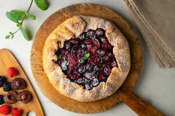 Galette tart with red berries, cherries, raspberries and blackberries. Top view table with christmas decoration.