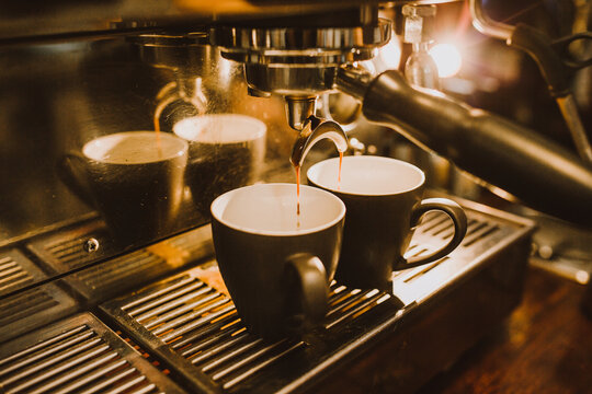 Shots of coffee dripping from machine into cups