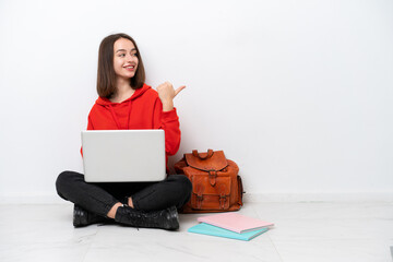 Young student Ukrainian woman sitting one the floor isolated on white background pointing to the...