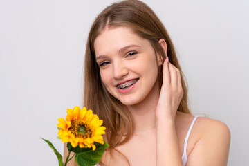 Teenager Russian girl isolated on white background holding a sunflower while smiling. Close up...