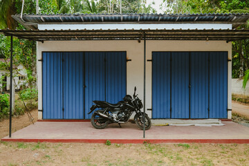 A black motorcycle is parked in front of a simple building with blue metal doors, surrounded by...