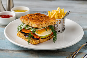 Gourmet vegetable sandwich with fresh herbs and fries on the side