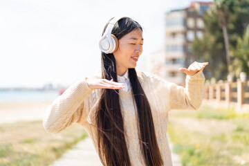 Young Chinese woman at outdoors listening music and dancing