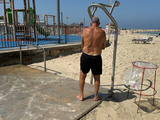 Man washes himself in shower on beach after swimming in sea. Beach equipped with open showers and...