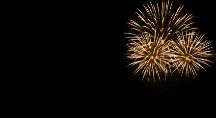 Fototapeta premium Golden bright explosive fireworks bursting against a deep black night sky, concept for celebration, holiday events and New Year's Eve party invitations