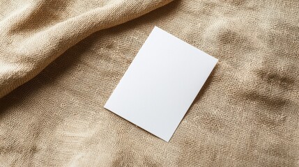A blank white card lies on textured beige fabric, ready for writing or design.