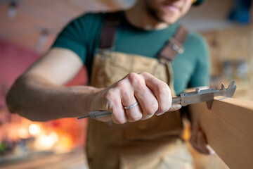 Close up of carpenter hands precisely measuring wood board thickness with calipers. Quality control, woodworking job, precision tools, material inspection, professional craftsmanship, detailed work