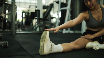 Close-up of a fit woman stretching her leg and hamstring on the gym floor