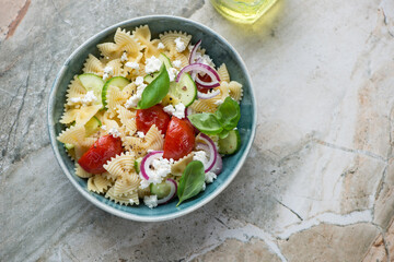 Bowl of farfalle pasta salad on a light-grey granite background, horizontal shot with space, flat lay