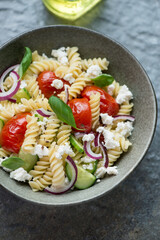 Pasta salad with fusilli, fresh cucumber, roasted tomatoes and cottage cheese, vertical shot on a dark-grey granite surface, middle close-up
