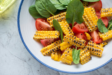 Close-up of salad with red tomatoes, grilled sweet corn and fresh spinach leaves in a white and blue plate, horizontal shot, selective focus