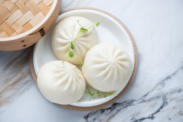 Plastic takeaway plate with panasian steamed baozi buns on a white stone background, horizontal shot, elevated view