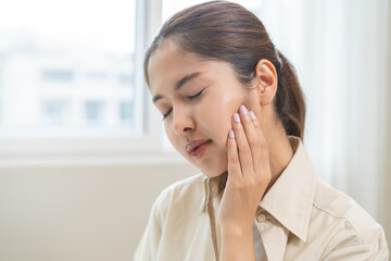Fototapeta premium Jaw pain, health care concept. Teeth pain and dentistry asian young woman, girl suffering touching her cheek. Female feeling painful toothache. Unhappy feel bad, diseases in oral, ache nerve and molar