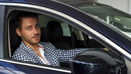 Happy man proudly sits in his new car, holding the keys