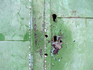Weathered green texture with visible holes and peeling paint showcasing the effects of time and exposure in an outdoor environment