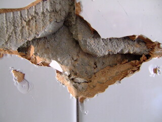 Damaged wall showcasing rough texture and exposed material layers in an interior setting during daylight hours