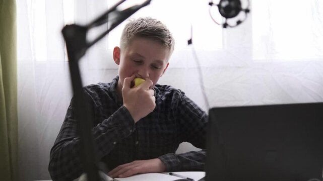 Teen boy eating apple at desk during online study session, healthy snack and remote learning theme
