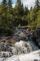 Norwegian mountain river with waterfalls where rapid water flows, creating white foam.