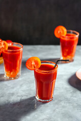 Three vegetable shaken cocktail in glass on dark grey background. Red tomato cocktail. Served with tomato slice. Vegan menu.