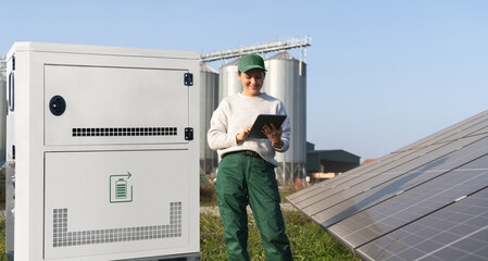 Farmer with digital tablet next to solar panels and energy storage. Farm using renewable energy. © scharfsinn86