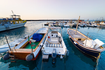 Wide angle shot of different types of boats, including wooden fishing boats, excursion vessels, and leisure boats, moored in the calm waters of Marina Grande, Capri island, Italy, at sunset